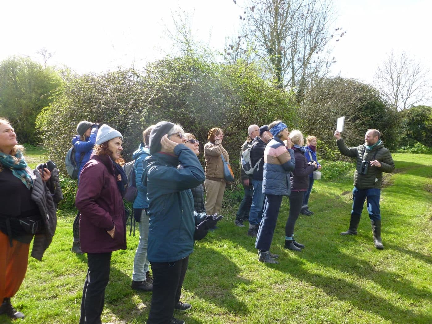 A group of people looking upwards through binoculars while standing in a grassy field